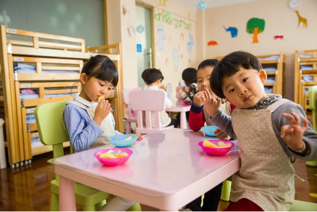 tiga kanak-kanak menikmati makanan ringan mereka di dalam bilik darjah